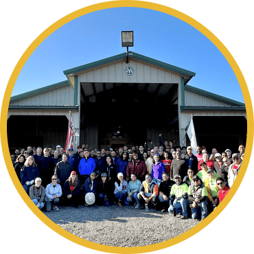 Large group of volunteers gathered in front of a farm warehouse for a group picture
