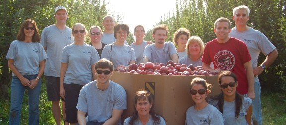 Smiling volunteers with a box of red apples in an orchard